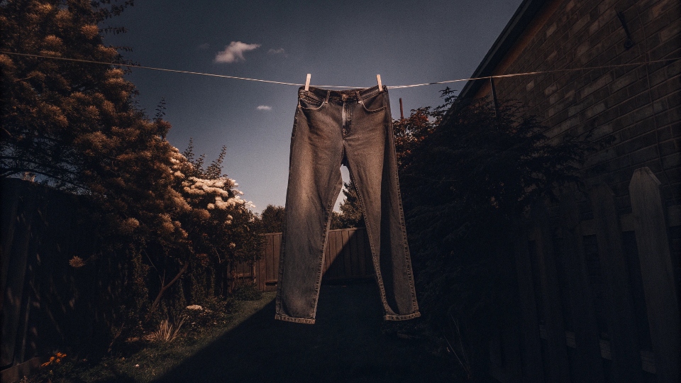A pair of jeans hanging on a clothesline outdoors to air dry.