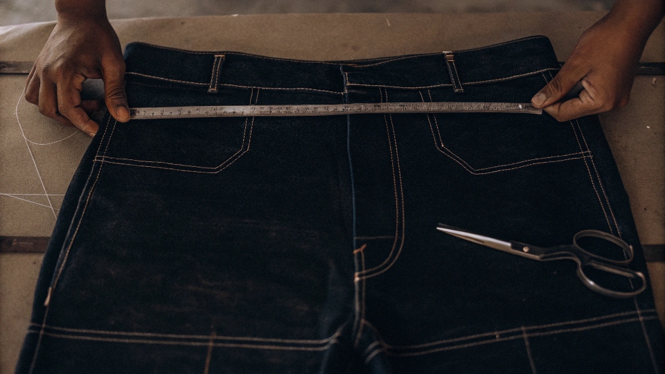 Measuring and marking a pair of jeans with chalk and a ruler before cutting them into shorts.