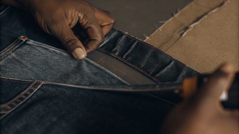 A hand applying fabric glue along the seam of a DIY denim skirt project.