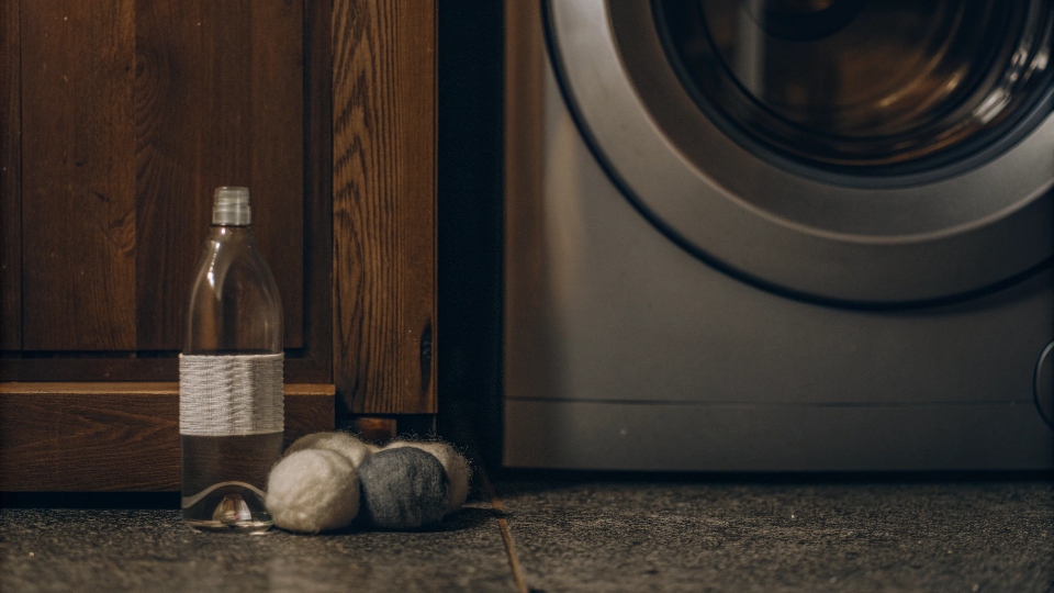 A bottle of white vinegar and wool dryer balls next to a washing machine.
