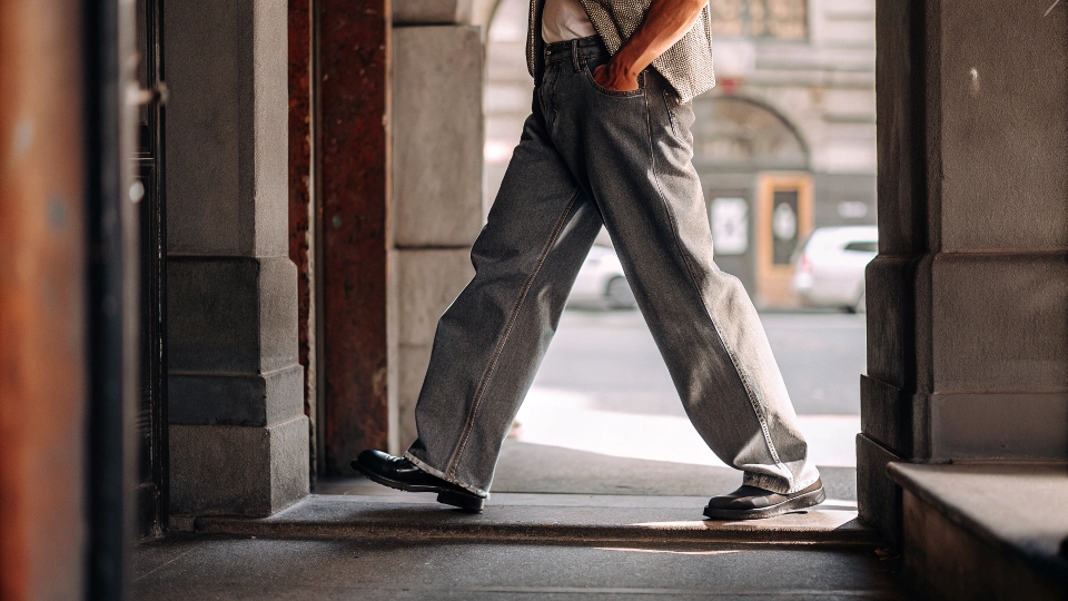 A stylish man wearing modern, well-fitting baggy jeans in a clean dark wash, looking fashionable in a city setting.