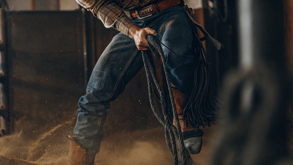 A close-up action shot of a rodeo cowboy, with the focus on the reinforced knee and seat of his Cinch jeans as he works.