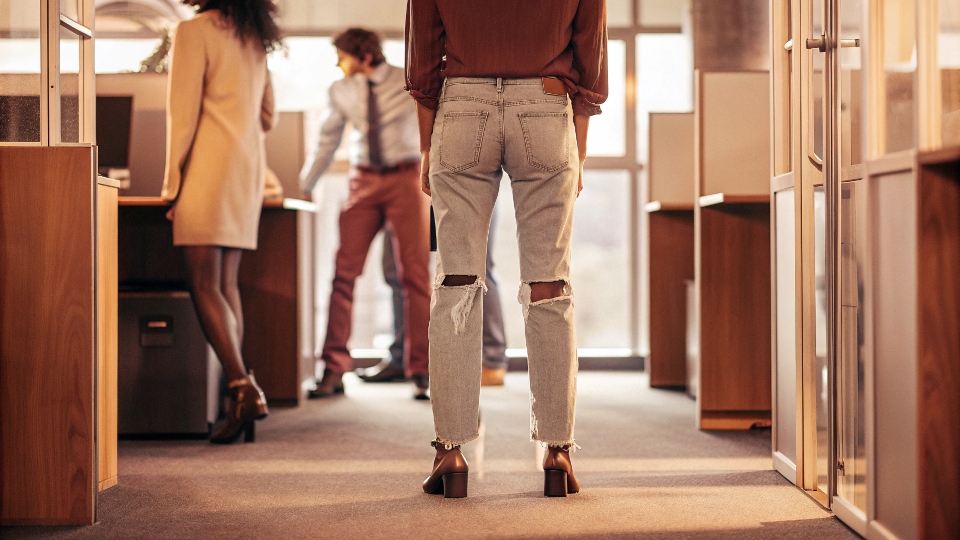 A person in ripped, light-wash baggy jeans looking out of place in a modern office environment.