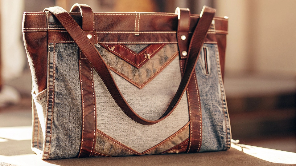 A stylish, finished handbag made from a pair of upcycled blue jeans, displayed against a clean background.