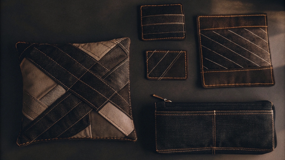 A beautiful flat lay of various items made from upcycled denim: a patchwork pillow, a set of coiled-seam coasters, and a small zippered pouch.
