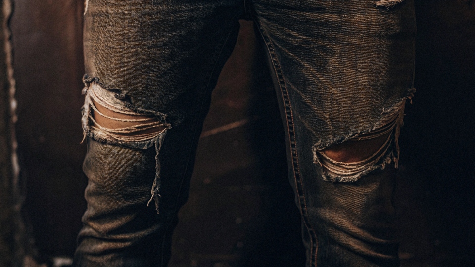A close-up shot of a pair of well-worn jeans with a significant rip in the crotch area.
