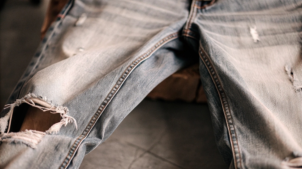 A pair of well-worn jeans with visible fraying and a hole in the inner thigh area.