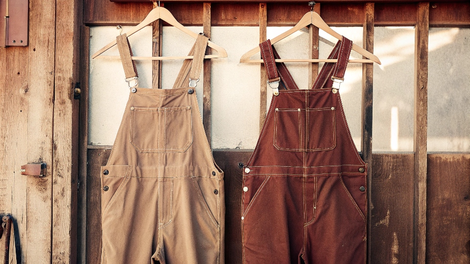 A classic pair of American-made bib overalls hanging on a rustic wooden wall