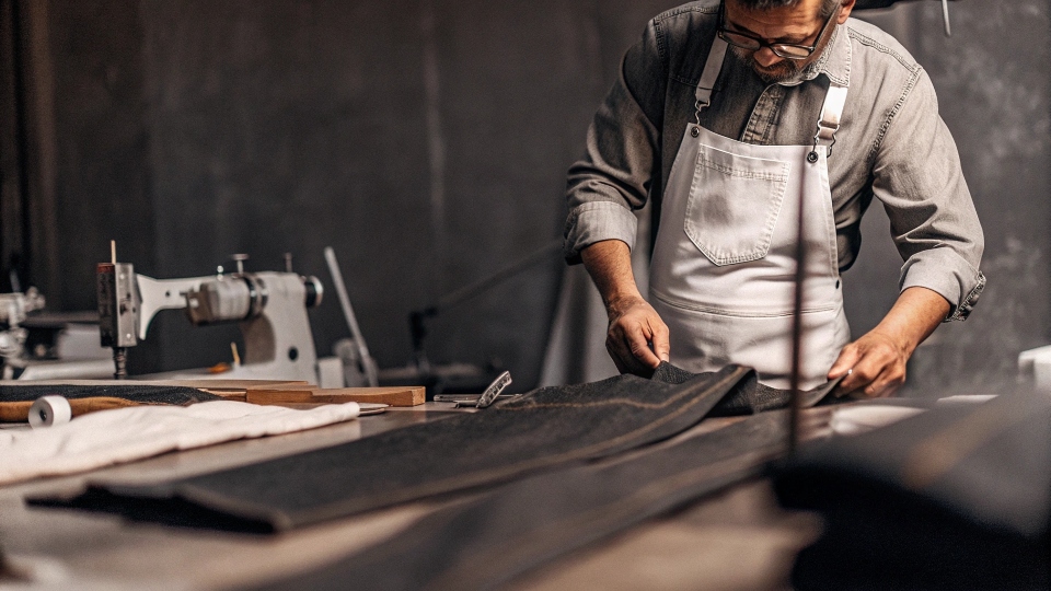 A master tailor measuring and crafting a single pair of custom jeans by hand in a workshop
