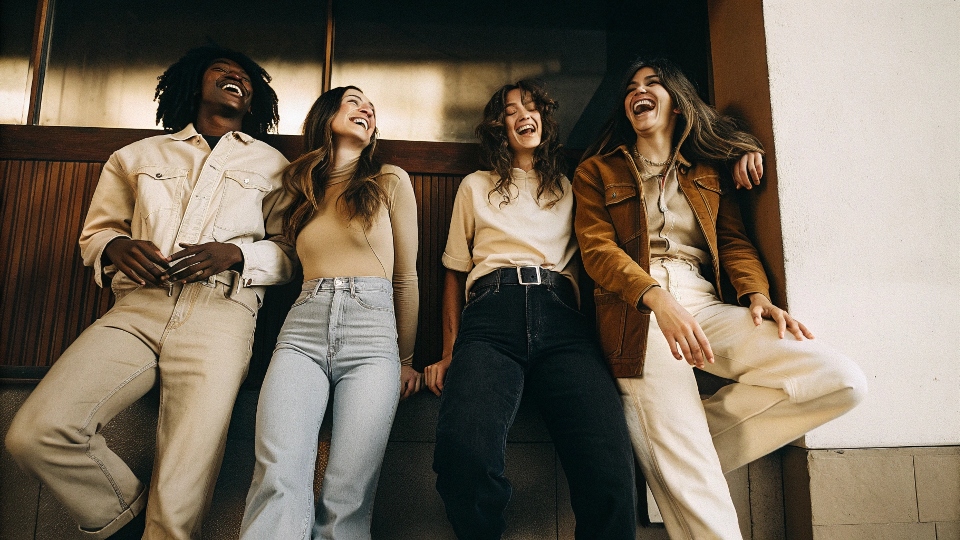 A diverse group of modern individuals laughing and posing in various styles of Calvin Klein jeans