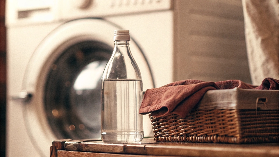 A bottle of white vinegar and a box of [baking soda](https://www.thespruce.com/baking-soda-and-laundry-odors-1900715)[^3] next to a washing machine