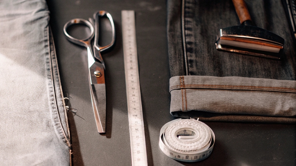 DIY tools for shortening jeans laid out: scissors, measuring tape, and [iron-on hem tape](https://diznewjeans.com/how-to-make-skinny-jeans-skinnier/)[^6]