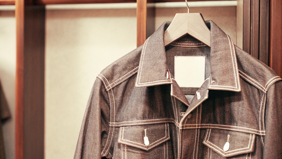 A classic denim jacket hanging on a wooden hanger against a clean background