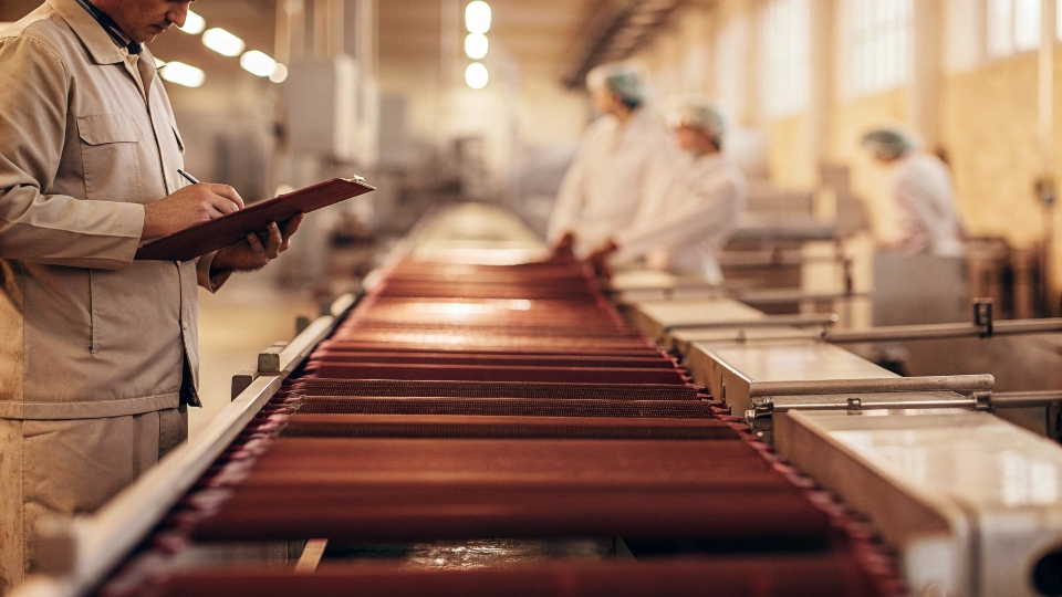 A government official inspecting a factory production line with a clipboard