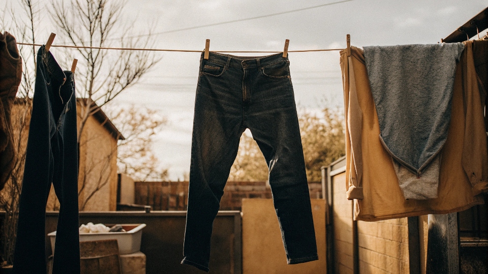 A person hanging their jeans inside-out on a clothesline to air dry