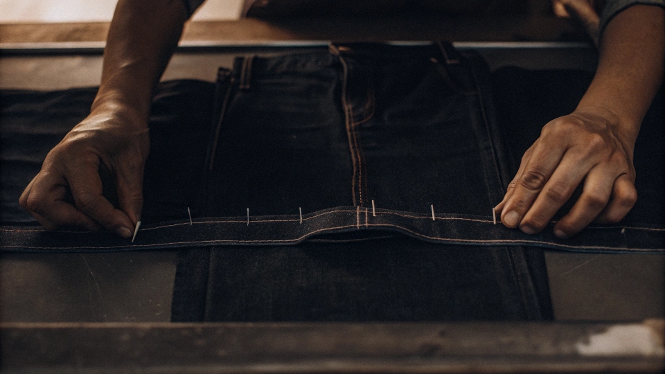 Professional Jean Tailoring and Alterations A tailor's hands pinning a pair of jeans for alteration on a sewing table
