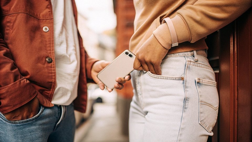 A person uncomfortably trying to fit their phone into the tiny, shallow front pocket of a pair of Nike jeans