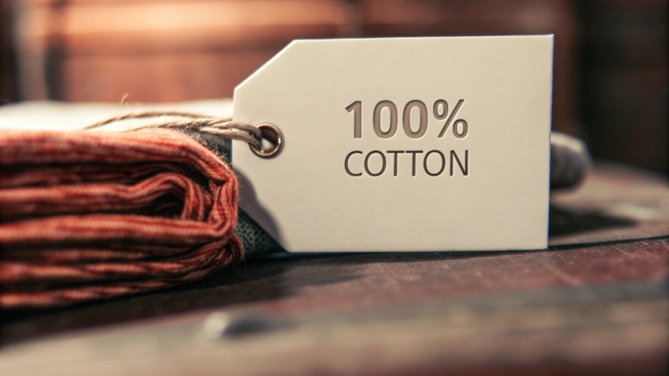 A close-up of a clothing tag showing "100% Cotton" next to a swatch of raw denim fabric
