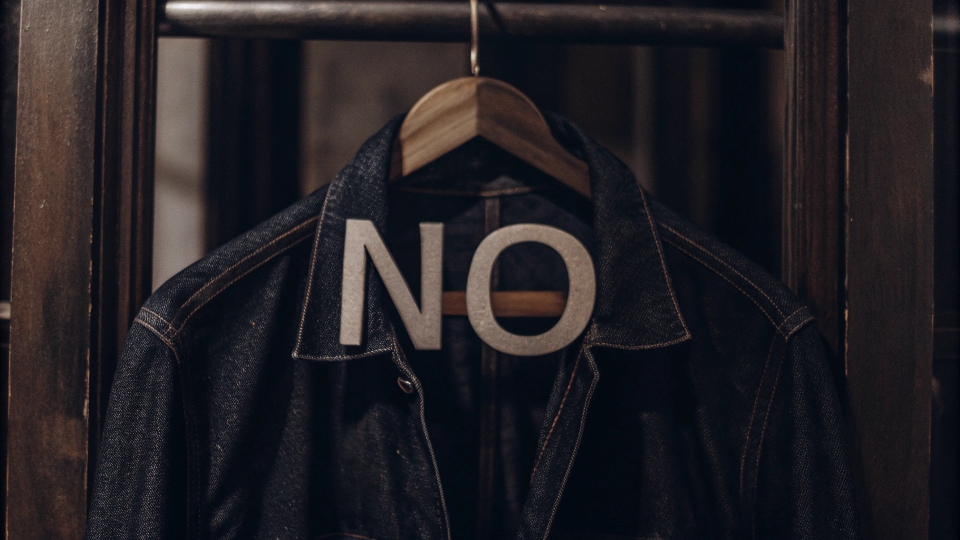 A universal "no" symbol placed over a dry cleaning hanger with a denim jacket