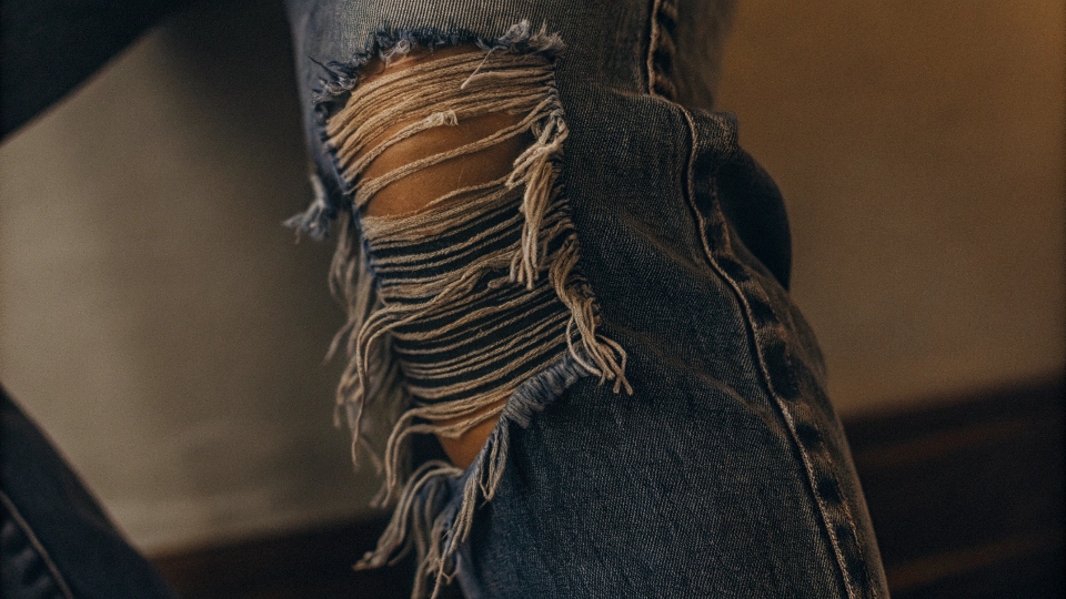 A close-up shot of the detailed fraying and texture on a ripped knee of a jean