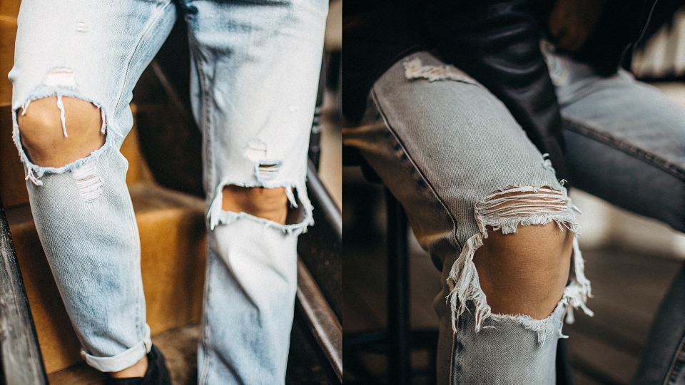 The Difference Between Ripped and Distressed Finishes on Denim A split image showing a close-up of a ripped knee on one side and a faded, worn thigh on the other