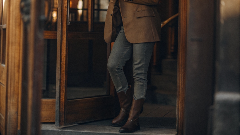 A person styling skinny jeans in a modern 2025 context, wearing them tucked into tall riding boots with an oversized blazer.