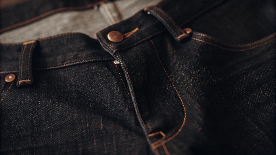 A close-up shot of dark-colored denim fabric, hinting at the dyes used in the process.