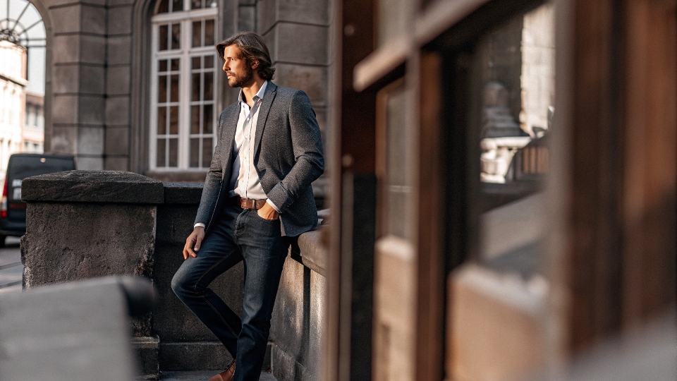 A man looking sharp and modern in a navy wool blazer, dark-wash jeans, and a simple button-down shirt