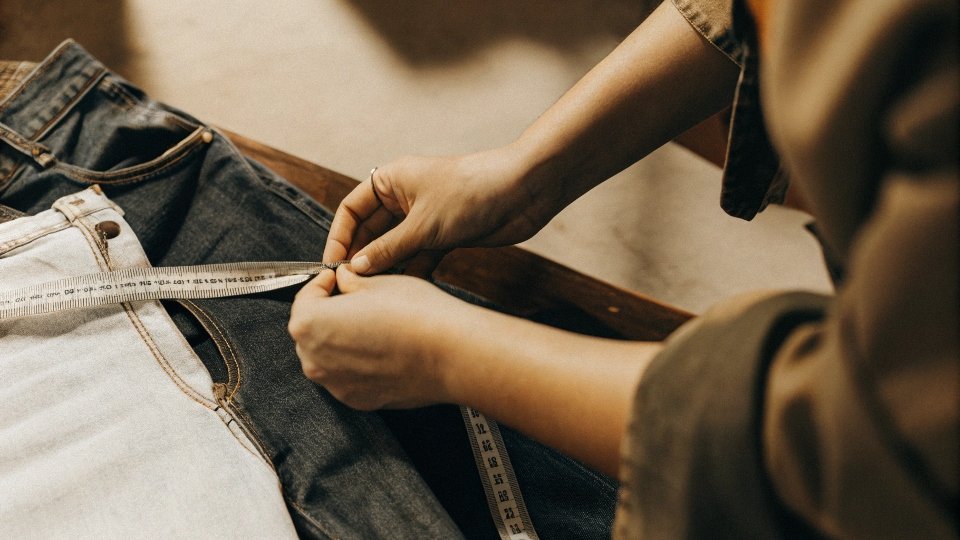A person measuring the inseam of a pair of jeans with a soft measuring tape