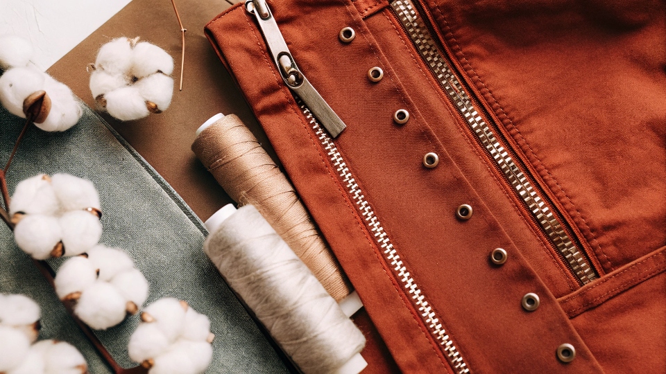 A flat lay of denim fabric, cotton bolls, [metal rivets](https://diznewjeans.com/what-components-does-it-take-to-make-levis-jeans/)[^5], a zipper, and spools of thread