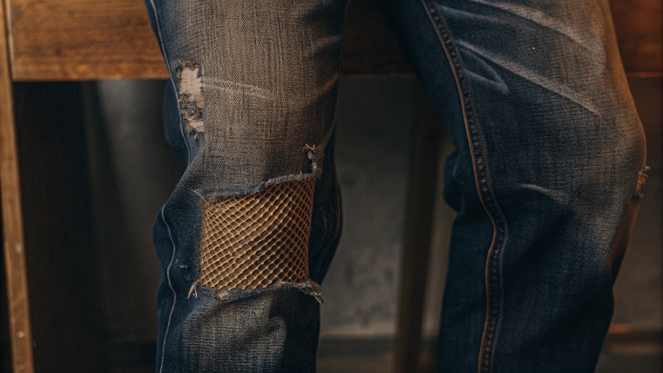 A close-up shot of the detailed "honeycomb" fades behind the knee of a pair of raw denim jeans
