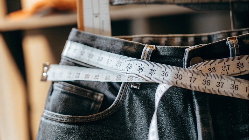 A close-up of a tape measure on a jeans waistband next to a size tag