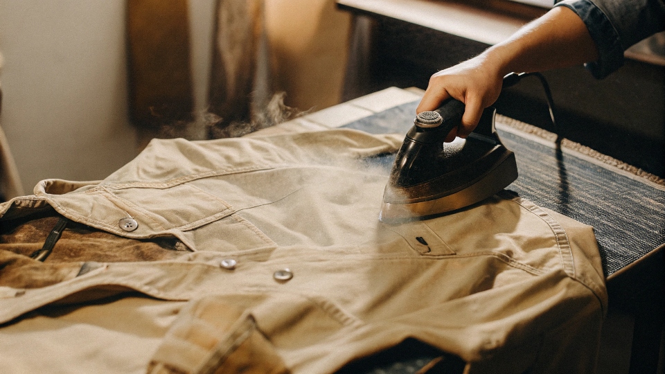 A person ironing the inside of a painted section of a denim jacket to heat-set the design