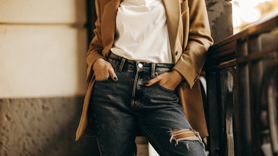 A stylish person wearing dark distressed jeans with a clean white t-shirt and a classic blazer