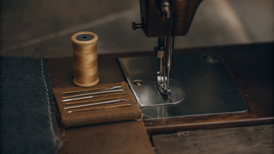 A standard home sewing machine with a spool of gold jeans thread and a package of denim needles next to it