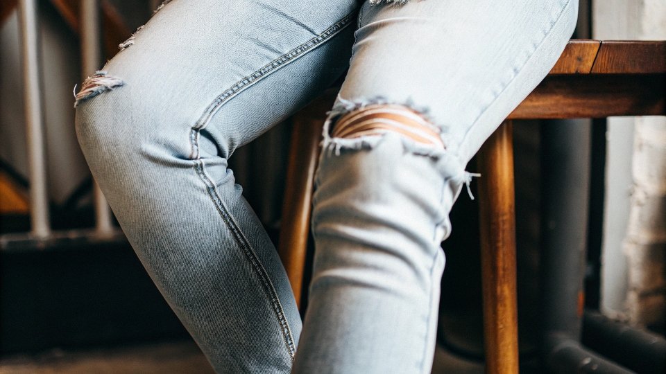 A close-up shot of a pair of modern distressed jeans showing a subtle, clean knee slit and light fraying