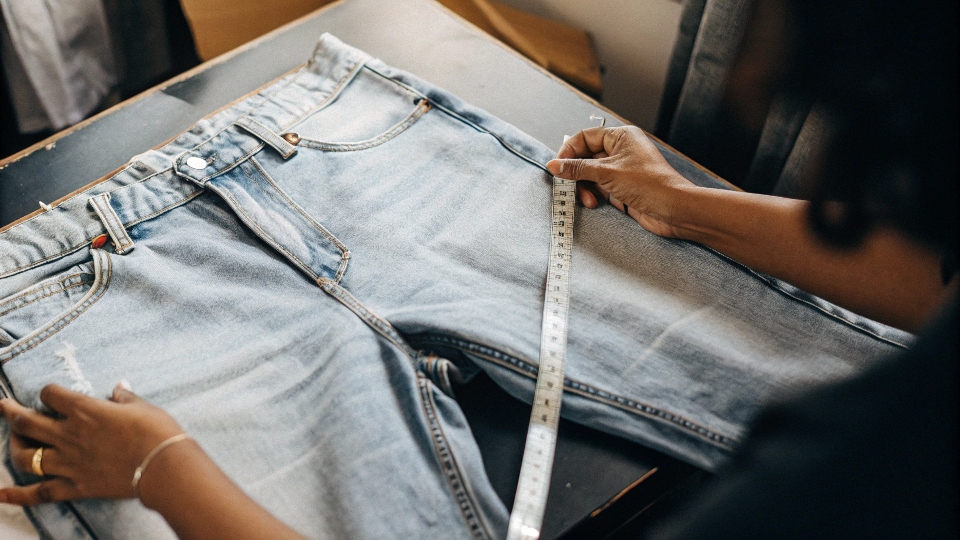 A person using a measuring tape to measure the waist of a pair of H&M jeans