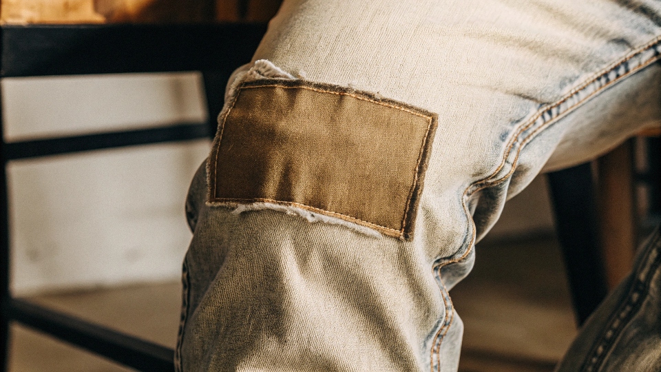 A close-up of a neat hand-stitched patch on the knee of a pair of worn jeans