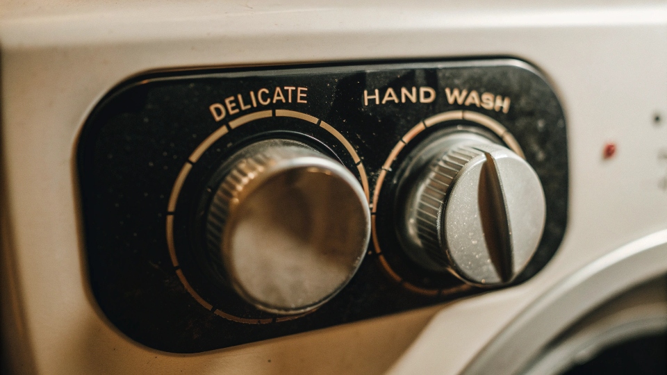 A close-up of a washing machine dial being turned to the "Delicate" or "Hand Wash" cycle with a cold temperature setting