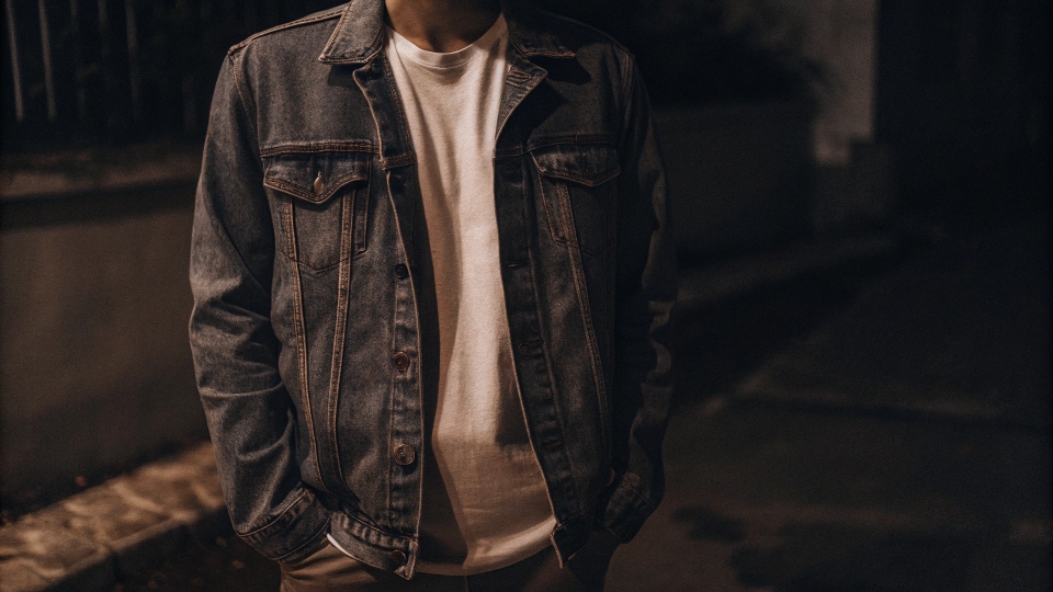 A person wearing a lightweight, light-wash denim jacket over a white t-shirt in the evening
