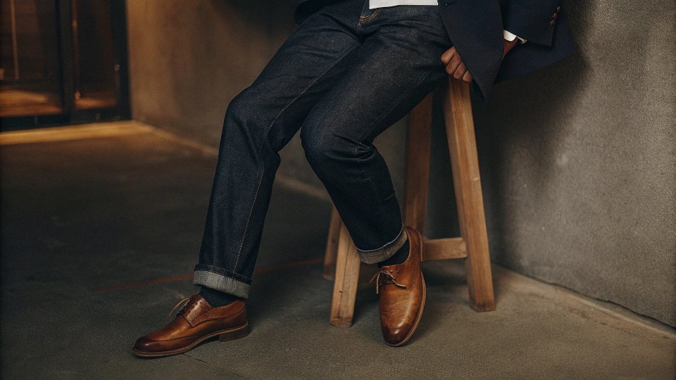 A person wearing dark jeans paired with a crisp white shirt, a tailored navy blazer, and brown leather loafers.