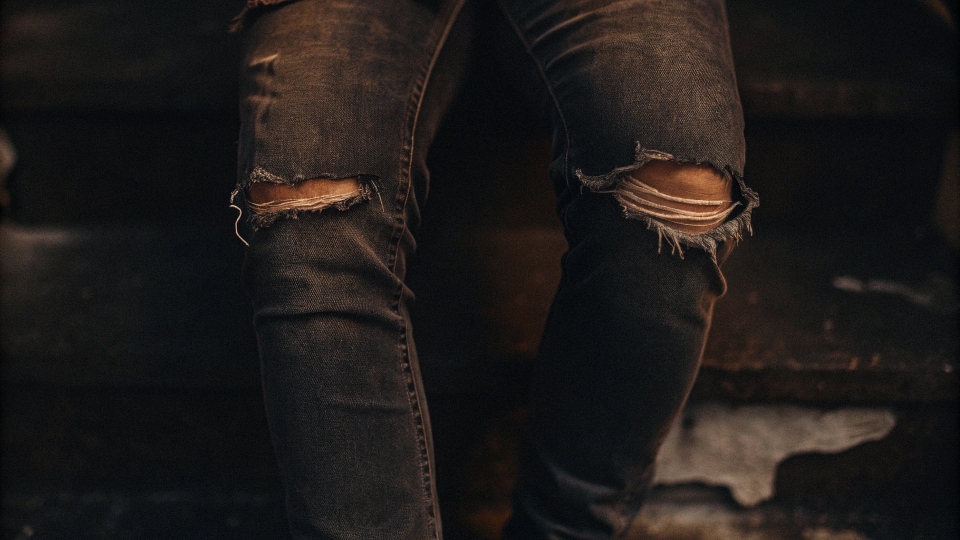 A close-up of a ripped crotch and faded knees on a pair of well-worn jeans