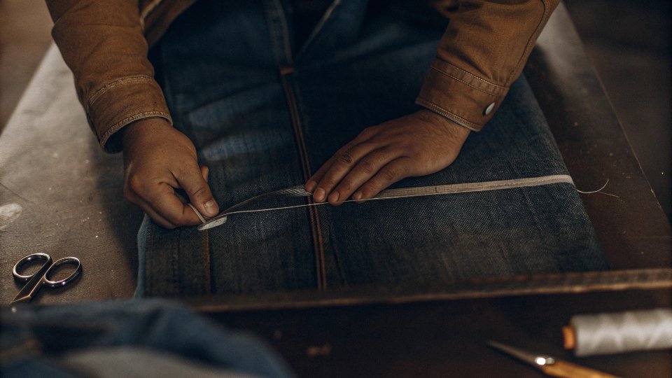 Marking Jeans for a Knee-Length Skirt A person using chalk to mark a straight cutting line above the knee on a pair of jeans