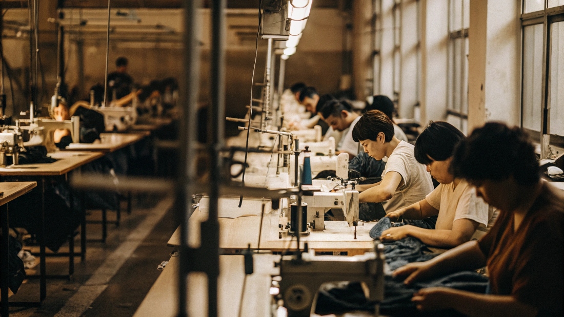 A long assembly line in a garment factory with multiple workers each performing a specific task