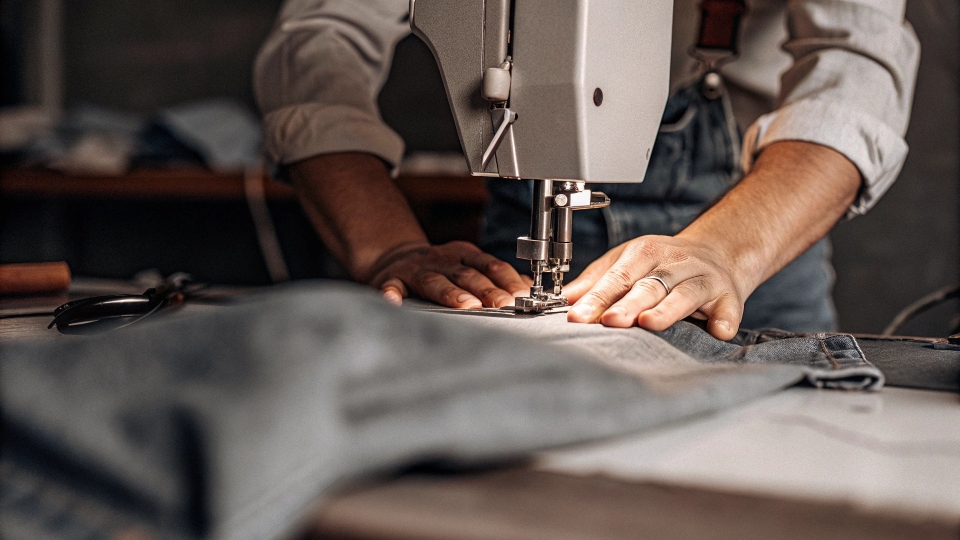 A tailor using a [sewing machine](https://diznewjeans.com/can-you-make-a-full-pair-of-jeans-with-a-small-sewing-machine/)[^6] to expertly alter the seam of a pair of jeans