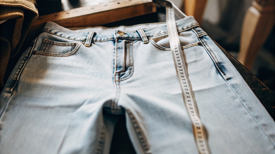 A pair of jeans laid flat with the long inseam highlighted by a measuring tape