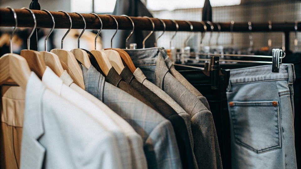 A clothing rack at a dry cleaner showing a mix of suits and jeans with alteration tags