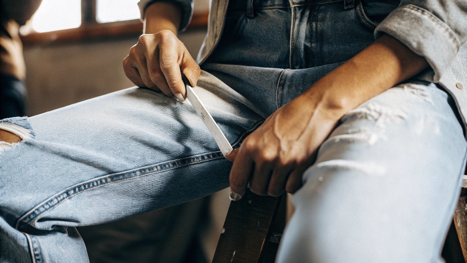 A person wearing jeans and using chalk to mark a line on their thigh for cutting