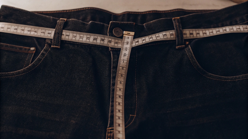 A close-up shot of a measuring tape stretched across the waistband of a pair of jeans laid flat
