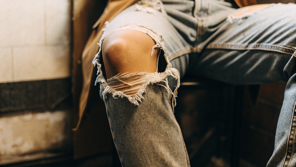 A close-up of a ripped knee on a well-worn pair of jeans